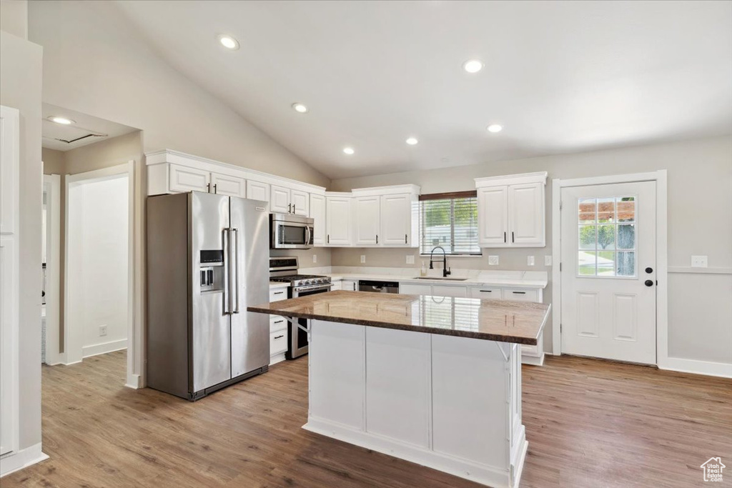 Kitchen with appliances with stainless steel finishes, a sink, white cabinetry, a kitchen island, and lofted ceiling