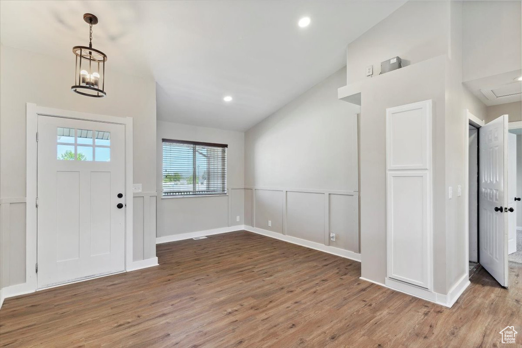 Foyer featuring lofted ceiling, wood finished floors, wainscoting, a decorative wall, and a chandelier
