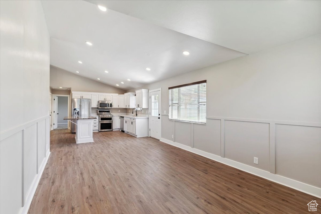 Unfurnished living room with a decorative wall, light wood finished floors, vaulted ceiling, recessed lighting, and wainscoting