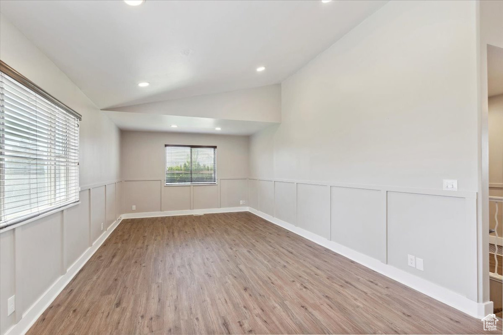 Empty room featuring vaulted ceiling, wood finished floors, recessed lighting, a decorative wall, and wainscoting