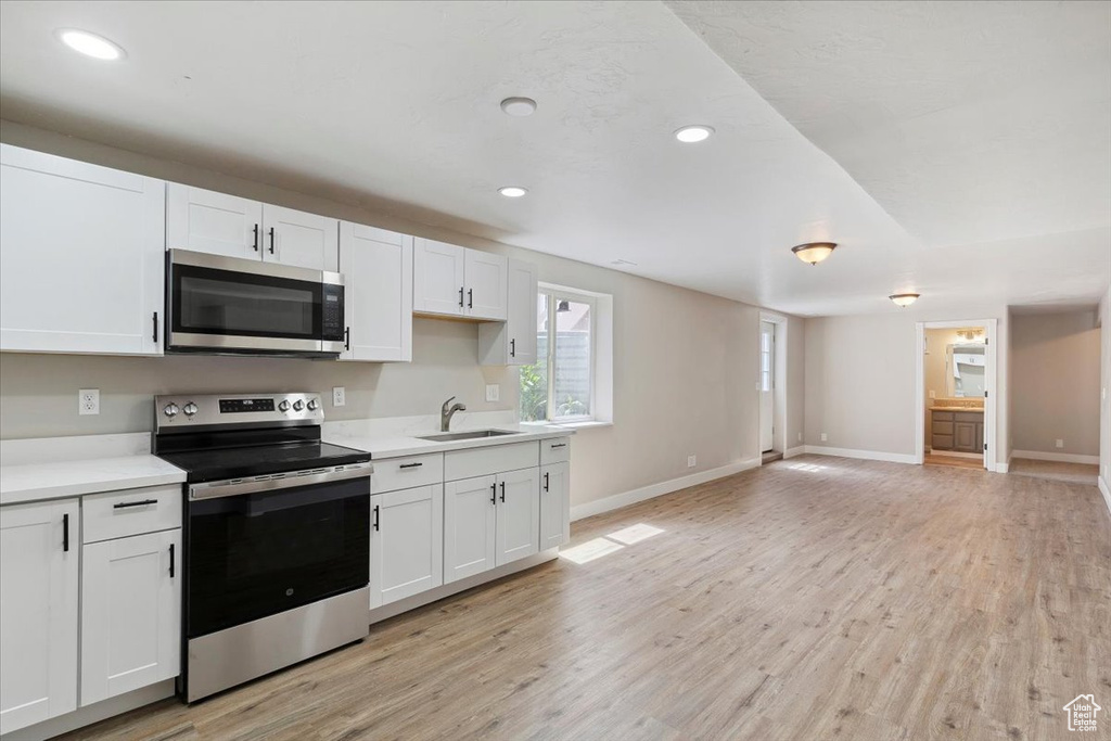 Kitchen featuring appliances with stainless steel finishes, a sink, light wood-style flooring, white cabinetry, and light countertops