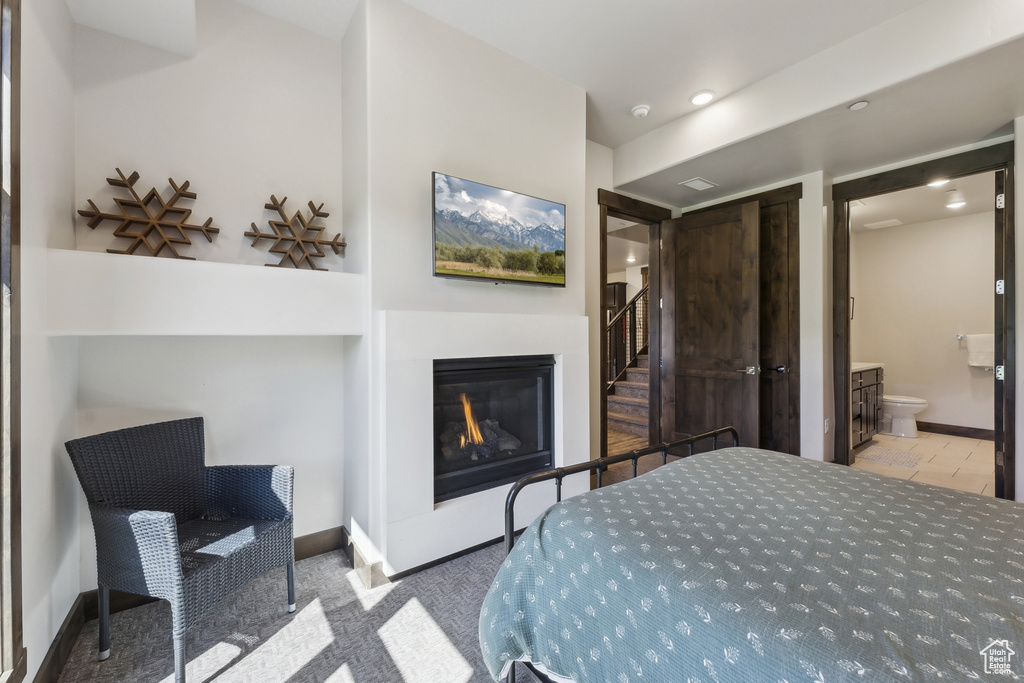 Carpeted bedroom featuring a glass covered fireplace, baseboards, a closet, ensuite bathroom, and recessed lighting