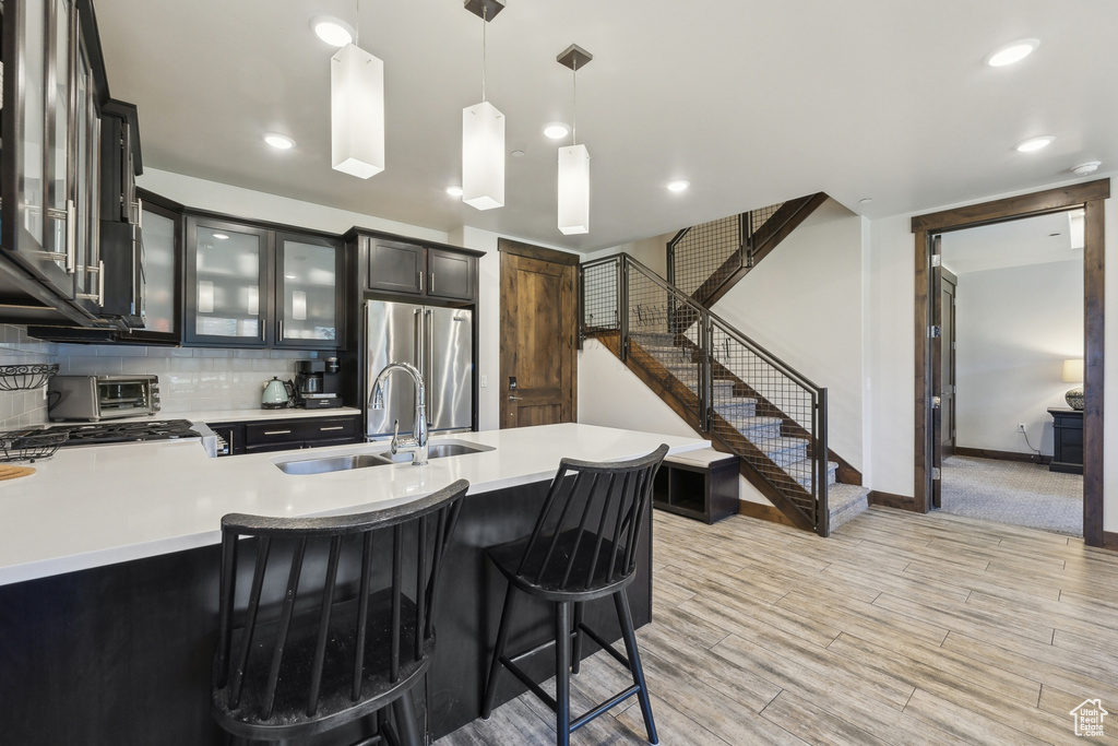 Kitchen featuring a sink, high quality fridge, light countertops, hanging light fixtures, and glass insert cabinets