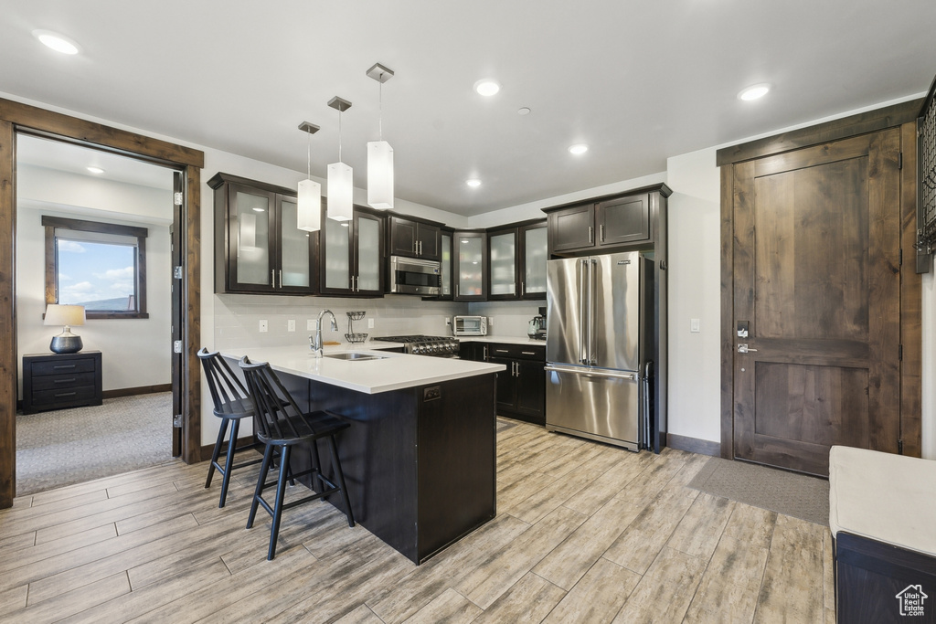 Kitchen with appliances with stainless steel finishes, glass insert cabinets, a peninsula, a sink, and baseboards