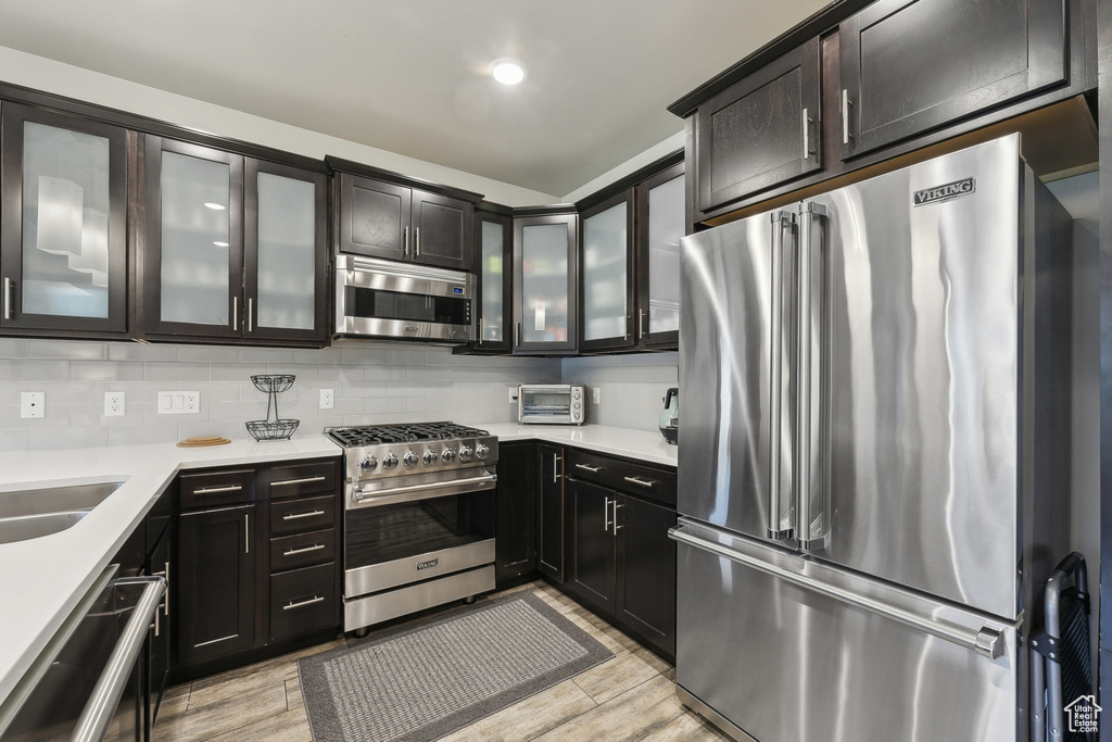 Kitchen with high quality appliances, light countertops, tasteful backsplash, light wood-type flooring, and glass insert cabinets