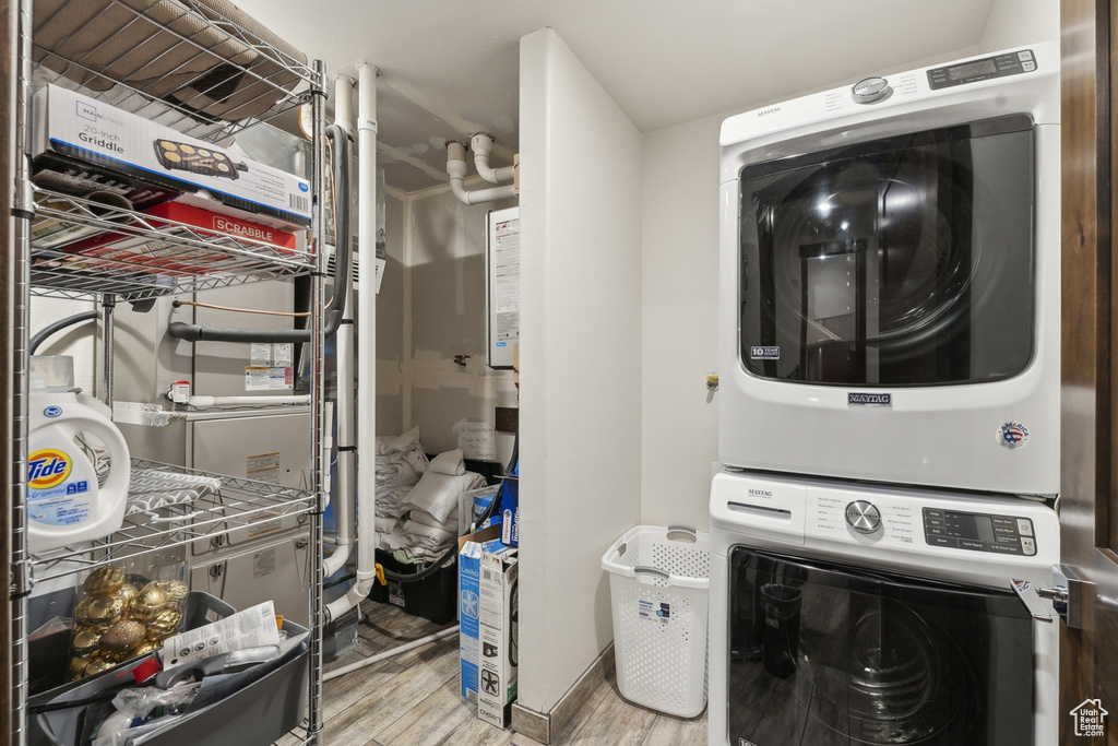 Clothes washing area featuring stacked washer and clothes dryer, wood finished floors, and heating unit