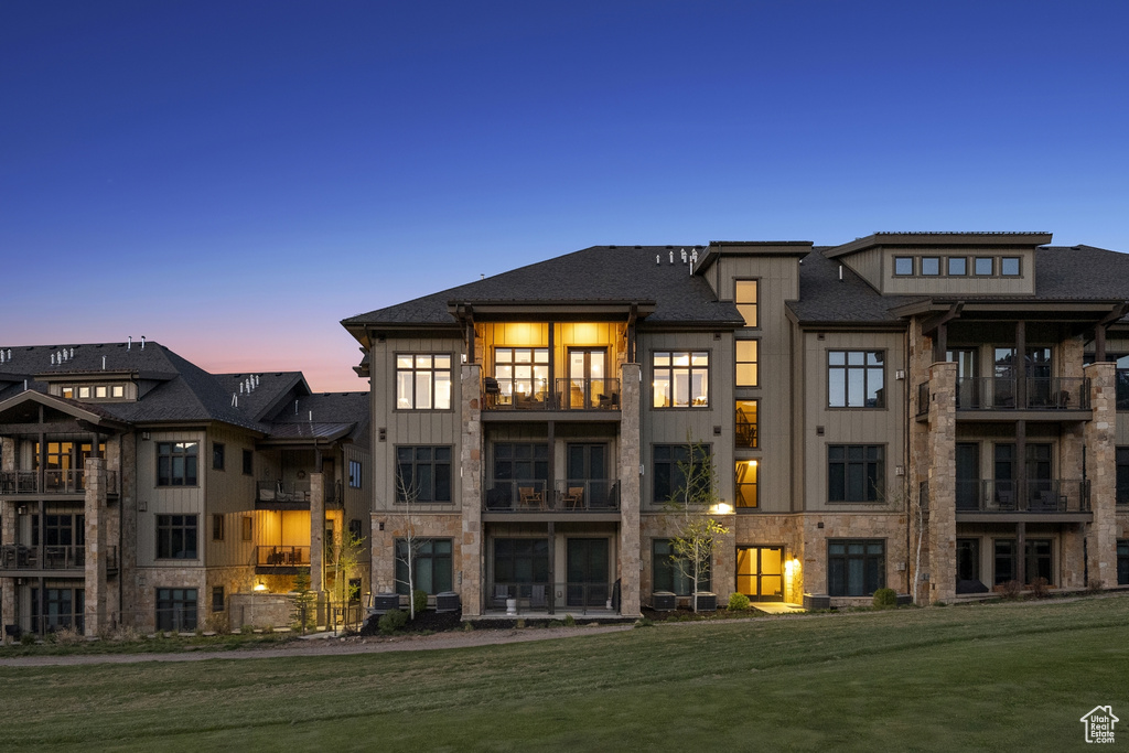 Back of property at dusk with board and batten siding, a lawn, and a balcony