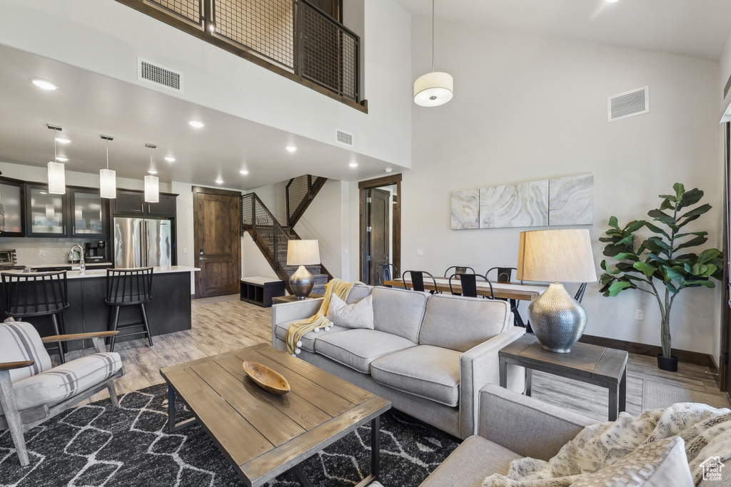 Living area featuring light wood-type flooring, high vaulted ceiling, stairs, recessed lighting, and baseboards