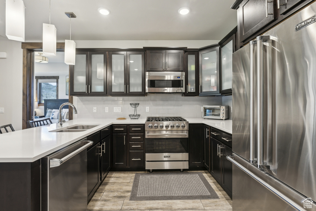 Kitchen featuring premium appliances, a sink, a peninsula, light countertops, and hanging light fixtures