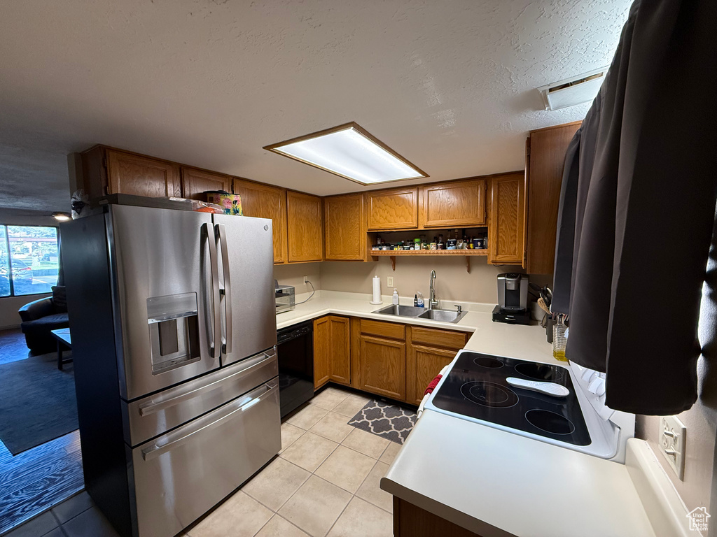 Kitchen featuring stainless steel fridge, a sink, black dishwasher, brown cabinets, and a textured ceiling