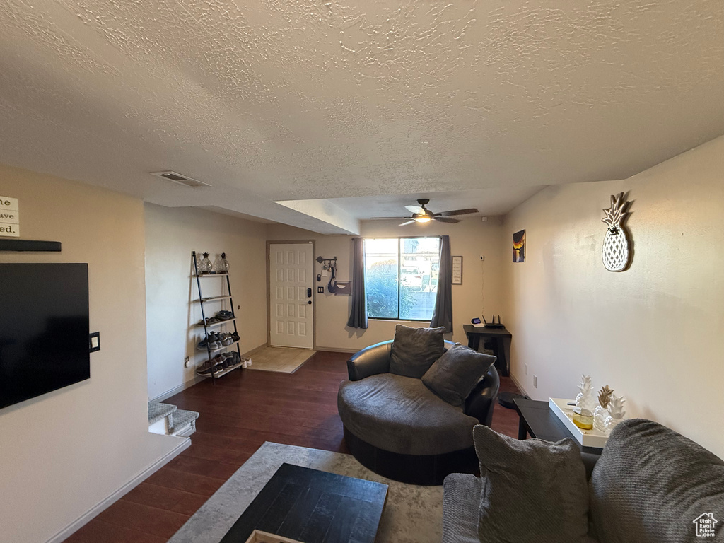 Living room with a textured ceiling, wood finished floors, ceiling fan, and baseboards