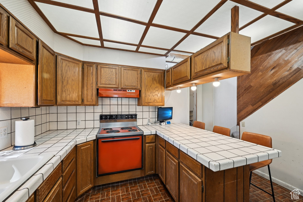 Kitchen featuring range with electric cooktop, tile counters, under cabinet range hood, and a peninsula