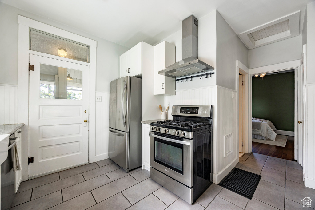 Kitchen with appliances with stainless steel finishes, wall chimney exhaust hood, wainscoting, light tile patterned flooring, and white cabinets