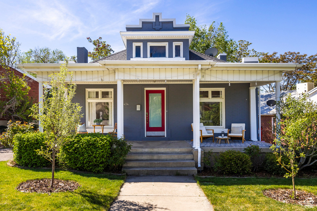 View of front of property with a chimney, a porch, a shingled roof, and board and batten siding