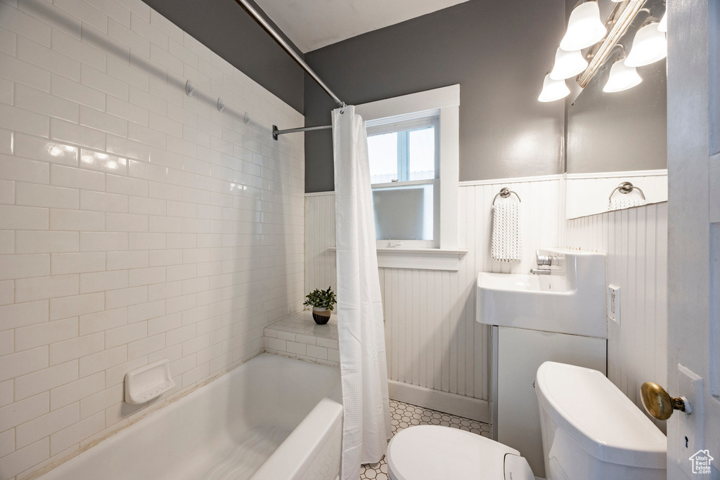 Full bath featuring toilet, shower / bath combo with shower curtain, wainscoting, a chandelier, and vanity