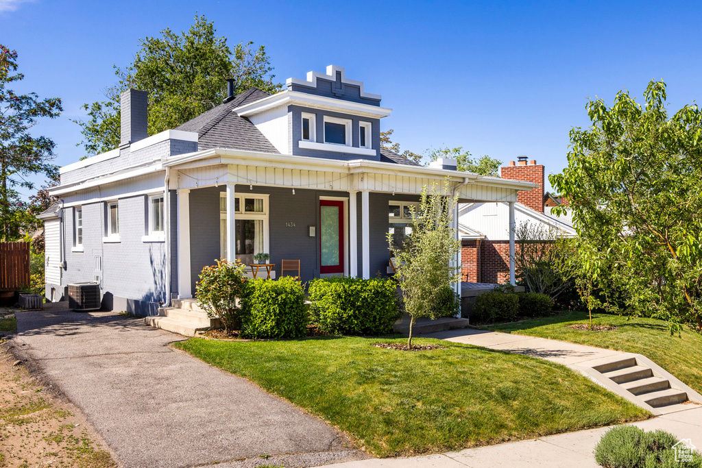 View of front of property featuring covered porch, a chimney, cooling unit, a front lawn, and brick siding