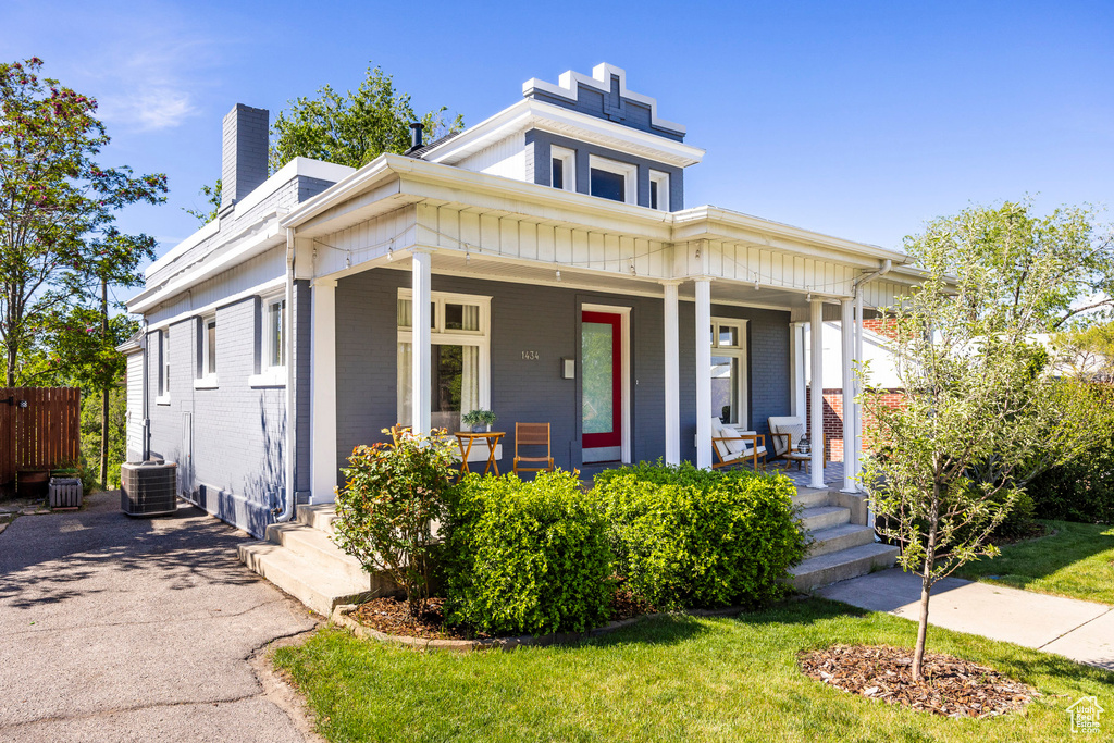 View of front of property with a porch, a chimney, brick siding, and cooling unit