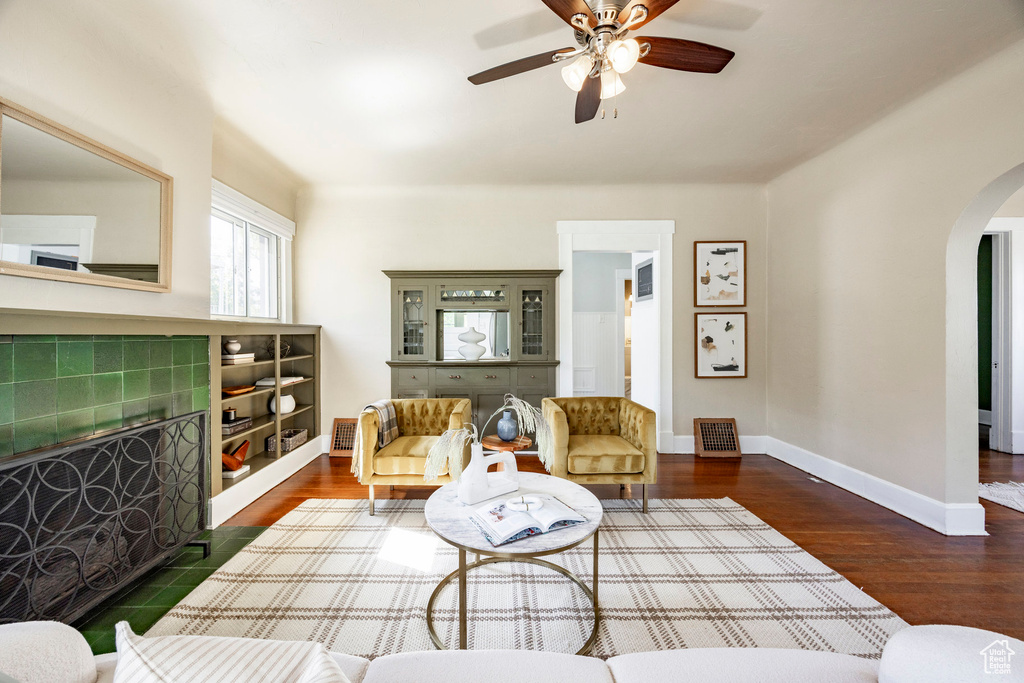 Living room with arched walkways, a ceiling fan, a fireplace, baseboards, and wood finished floors