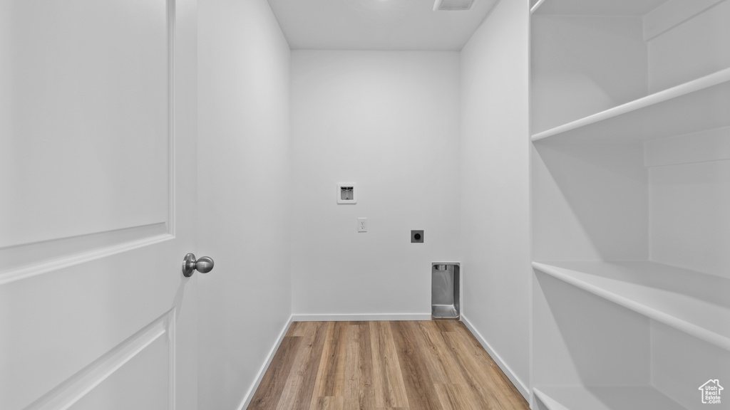 Clothes washing area with hookup for an electric dryer, washer hookup, wood finished floors, and baseboards