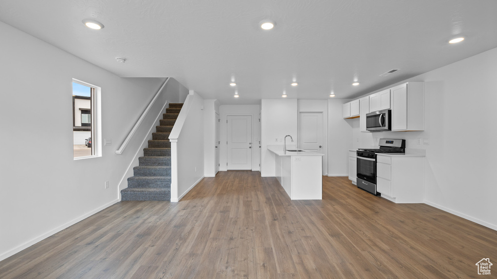 Kitchen with appliances with stainless steel finishes, a sink, baseboards, wood finished floors, and recessed lighting