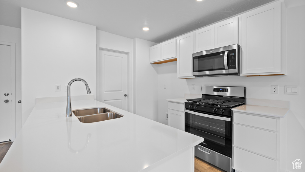 Kitchen with stainless steel appliances, a sink, light wood finished floors, white cabinetry, and recessed lighting