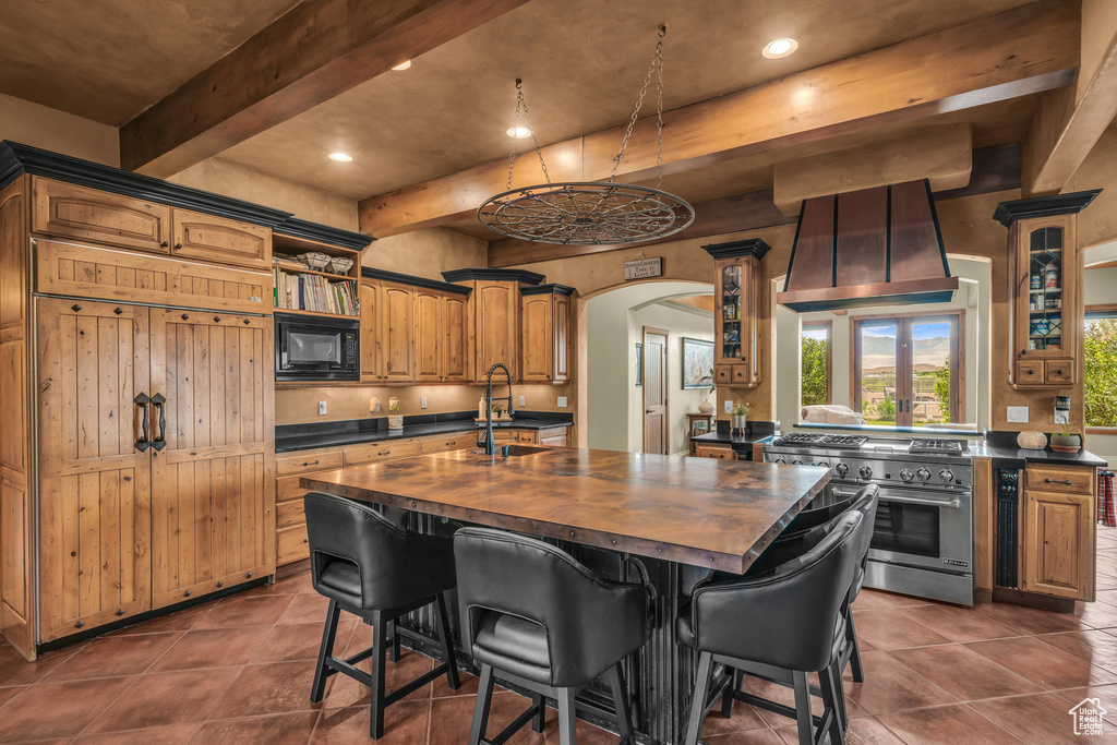 Kitchen featuring range with two ovens, black microwave, butcher block counters, a sink, and beam ceiling