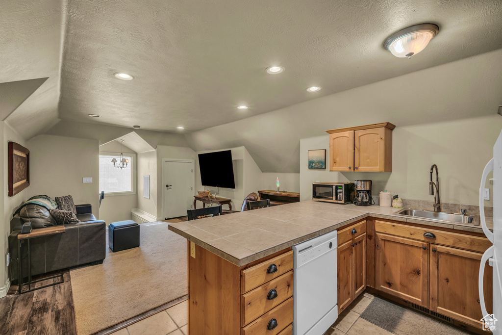 Kitchen featuring white appliances, open floor plan, a sink, a peninsula, and vaulted ceiling