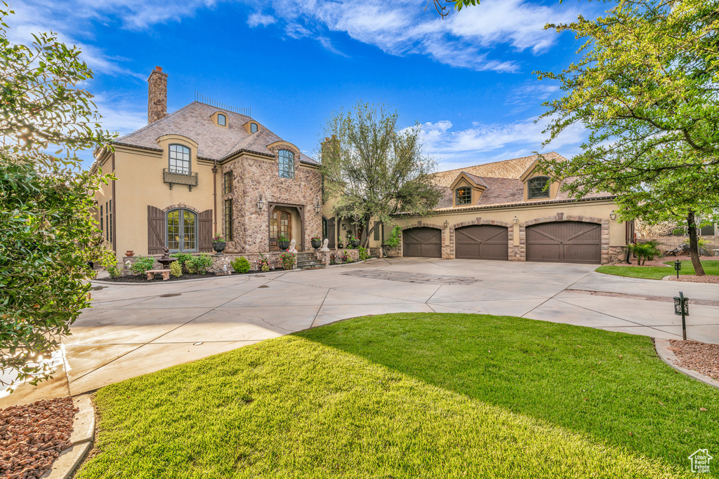 French country home featuring stone siding, driveway, a chimney, and a front lawn