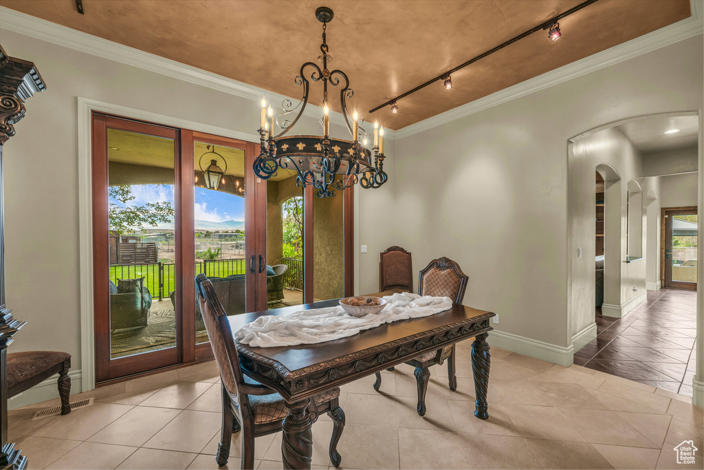 Dining area with arched walkways, ornamental molding, light tile patterned floors, track lighting, and a chandelier