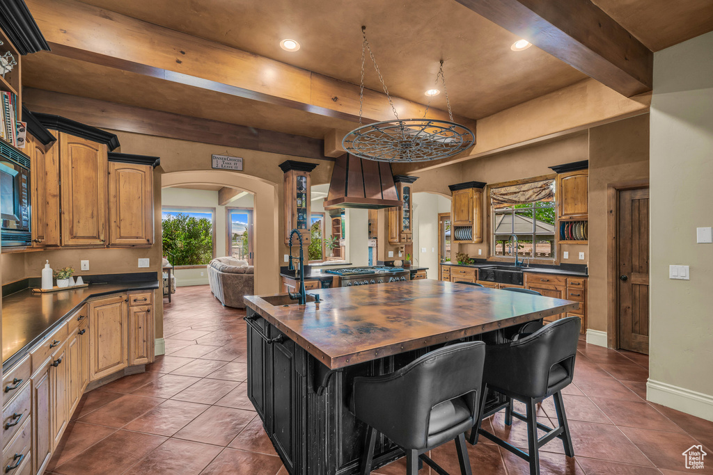 Kitchen with a sink, wood counters, arched walkways, custom exhaust hood, and beamed ceiling