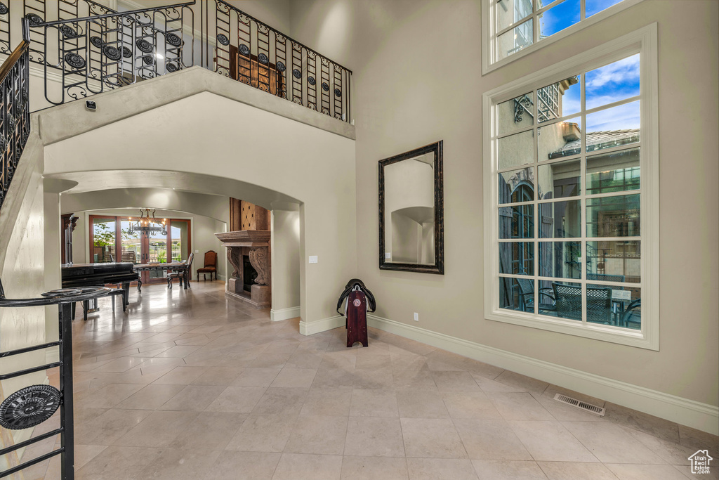 Tiled entrance foyer featuring arched walkways, a chandelier, baseboards, a fireplace, and a towering ceiling