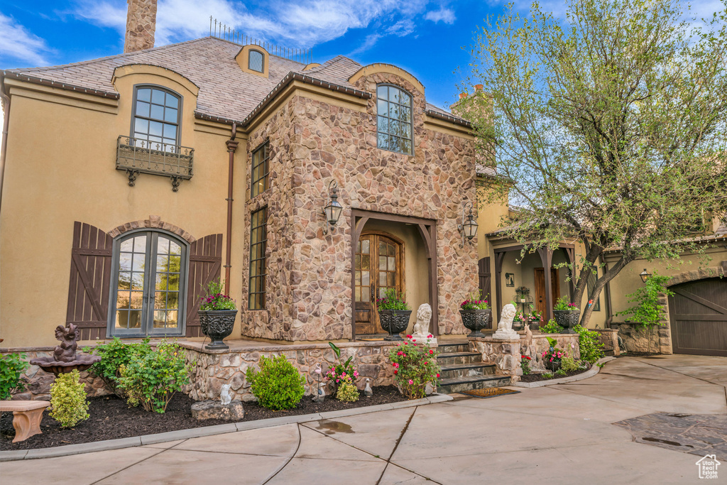 View of front of house with a chimney, driveway, stucco siding, and stone siding