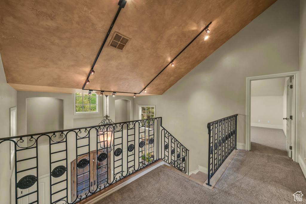 Hall featuring track lighting, an upstairs landing, carpet flooring, baseboards, and arched walkways