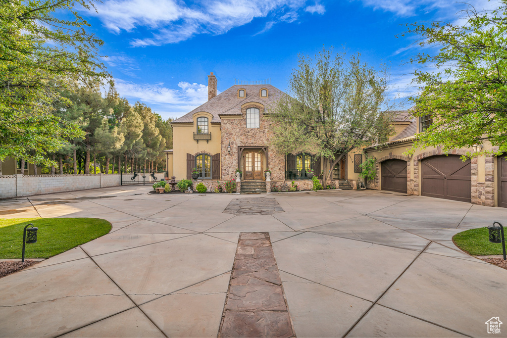 French country home featuring a chimney, driveway, fence, stucco siding, and stone siding