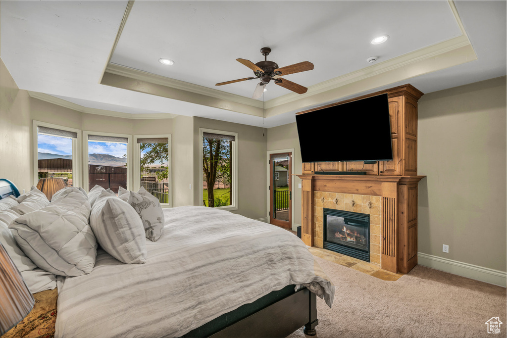 Bedroom with a tray ceiling, crown molding, light carpet, a tile fireplace, and recessed lighting