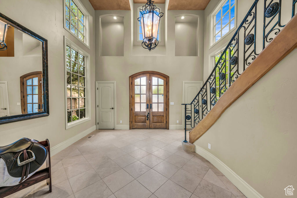 Tiled foyer featuring a chandelier, a towering ceiling, french doors, and healthy amount of natural light