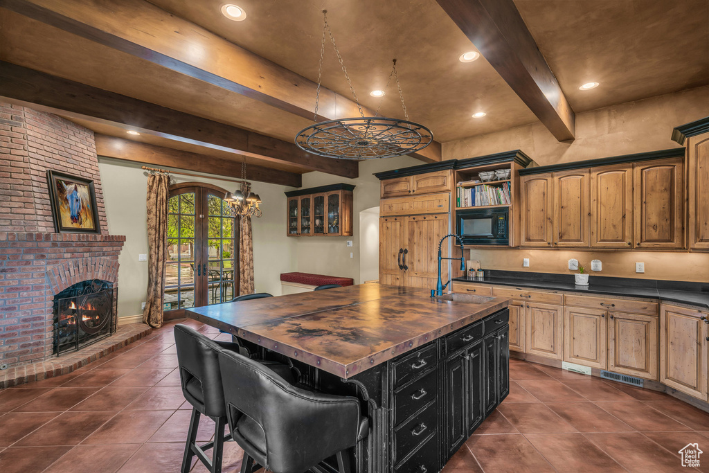 Kitchen with a sink, wood counters, dark tile patterned floors, black microwave, and beamed ceiling