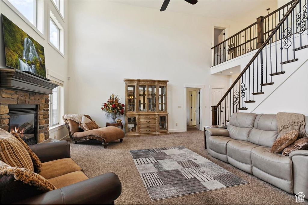 Carpeted living area featuring a high ceiling, plenty of natural light, a ceiling fan, a fireplace, and stairway