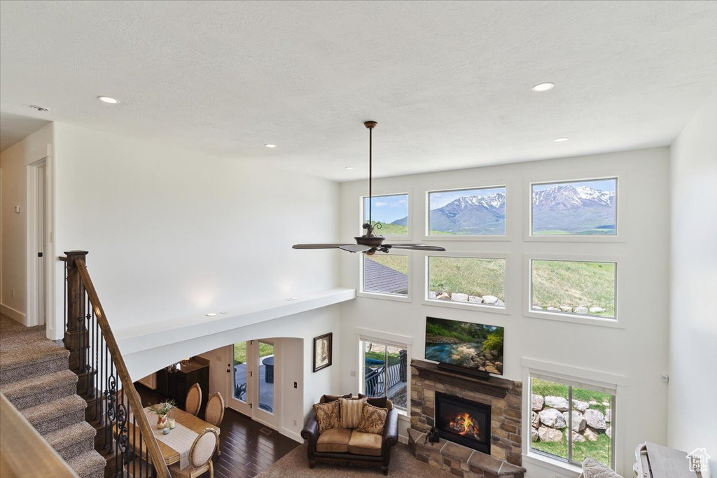 Living room with dark wood finished floors, a fireplace, ceiling fan, healthy amount of natural light, and a high ceiling