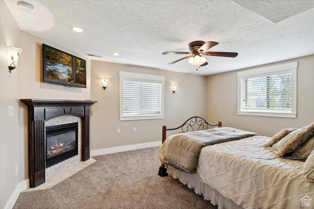 Bedroom with a textured ceiling, carpet flooring, a fireplace with flush hearth, baseboards, and a ceiling fan