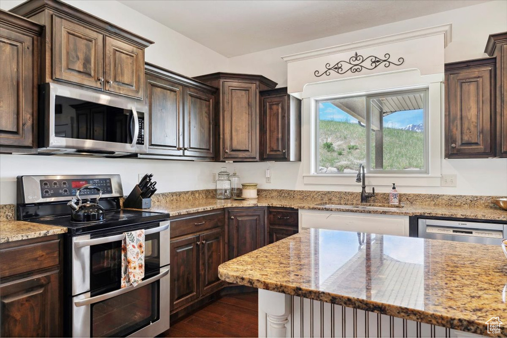 Kitchen featuring appliances with stainless steel finishes, a sink, dark brown cabinetry, and light stone countertops
