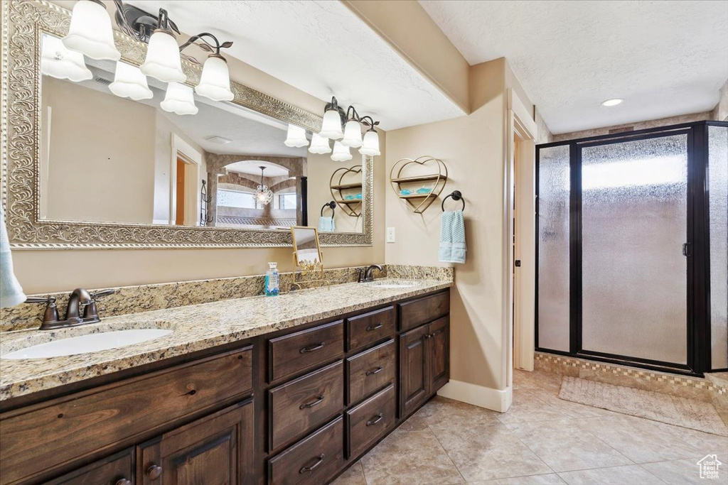 Full bathroom featuring a stall shower, double vanity, baseboards, a textured ceiling, and tile patterned floors