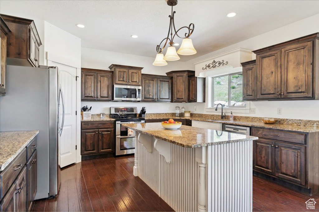 Kitchen featuring appliances with stainless steel finishes, a center island, dark brown cabinets, dark wood-style floors, and a sink