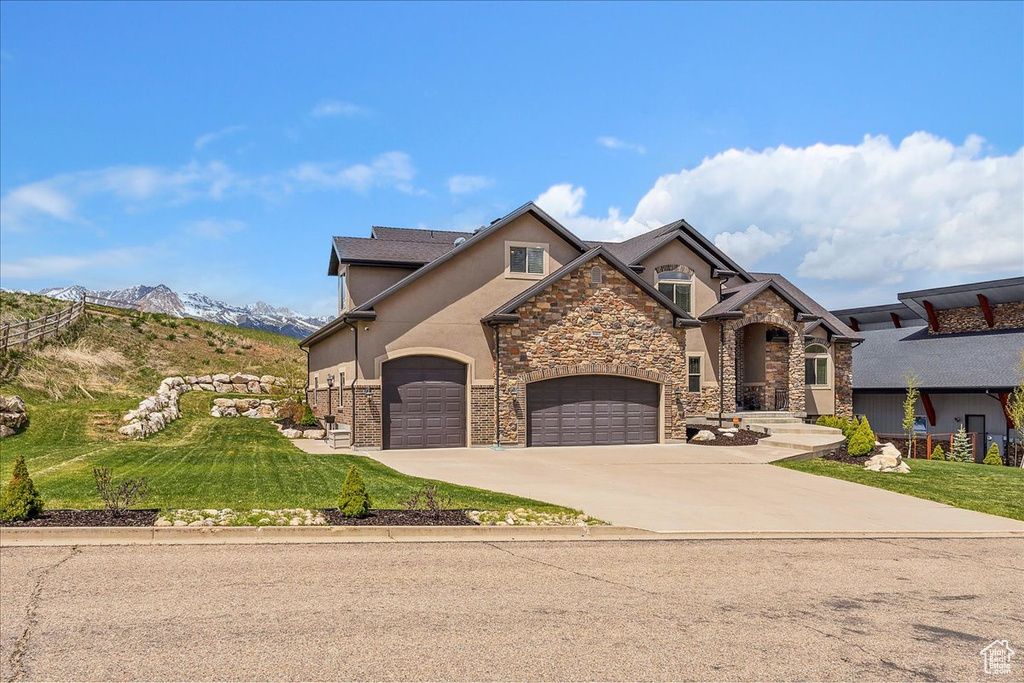 View of front of house featuring stucco siding, driveway, stone siding, and a front lawn