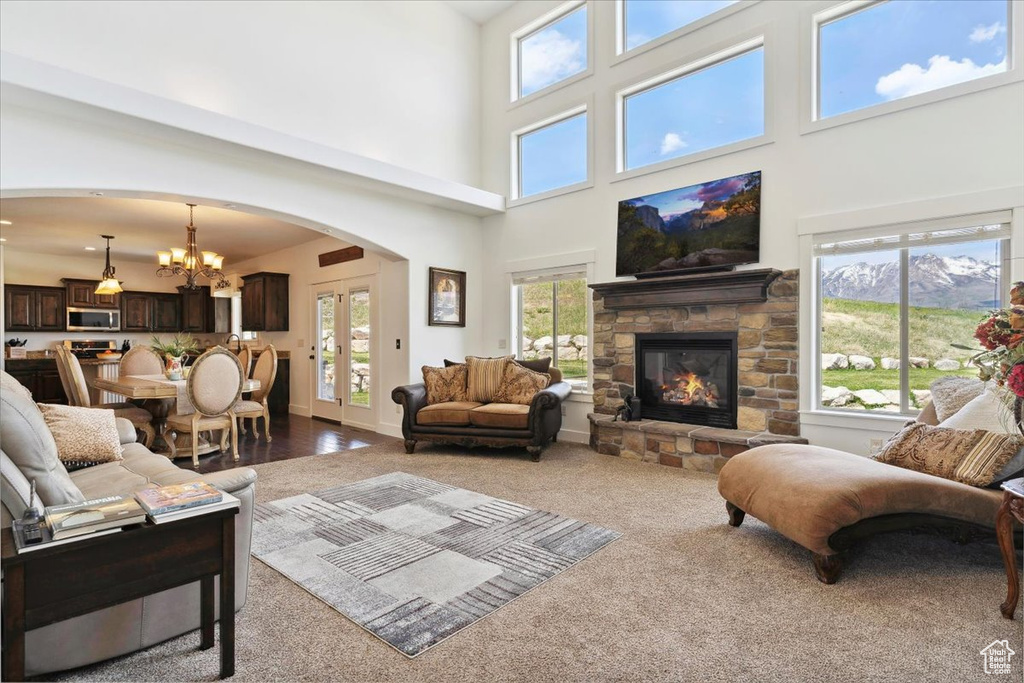 Carpeted living area featuring arched walkways, a stone fireplace, a chandelier, and a towering ceiling