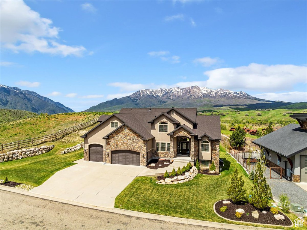 View of front of home with stone siding, a mountain view, an attached garage, driveway, and stucco siding