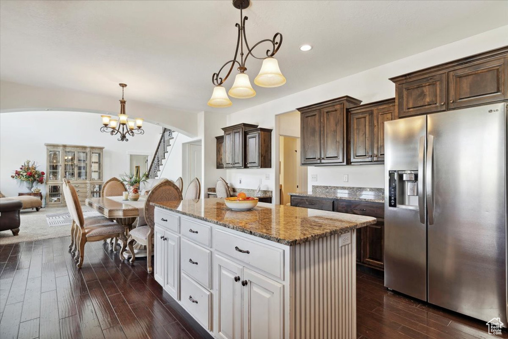 Kitchen featuring stainless steel refrigerator with ice dispenser, a center island, arched walkways, dark brown cabinetry, and dark wood-style floors