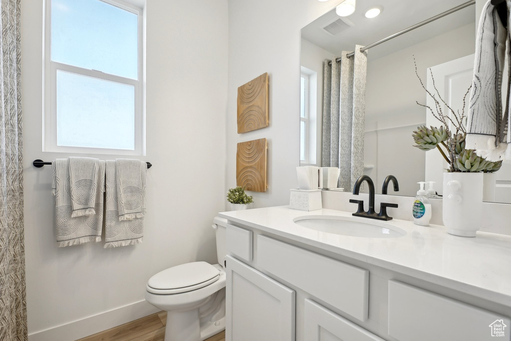 Full bath with plenty of natural light, toilet, vanity, and wood finished floors