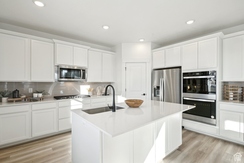 Kitchen featuring stainless steel appliances, a sink, backsplash, white cabinets, and light wood-style flooring