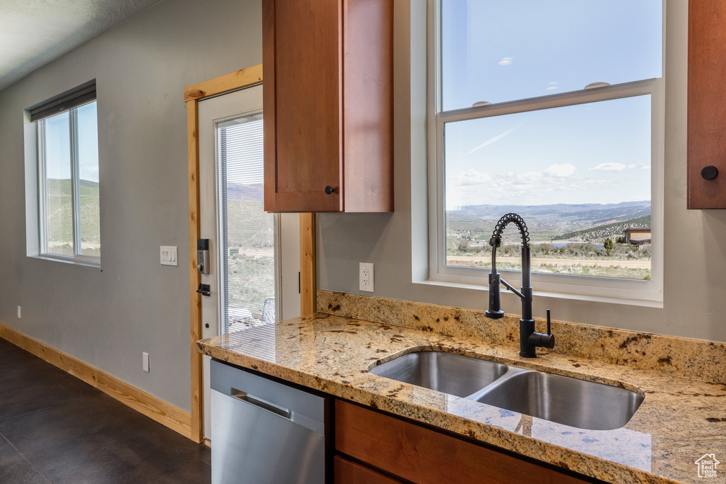 Kitchen featuring a sink, dishwasher, brown cabinetry, and light stone countertops